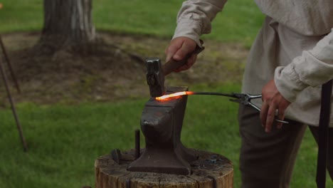 a revolutionary war reinacter blacksmith hammers out a hot piece of molten metal out on an anvil