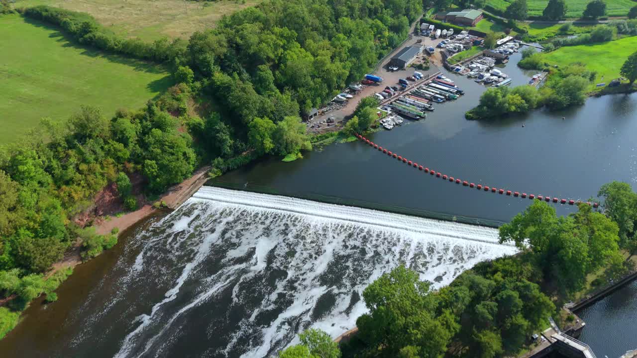 Flying drone over Gunthorpe Weir and River Trent in Nottinghamshire England with navigation canal, rural farmland and glowing summer sunset horizon