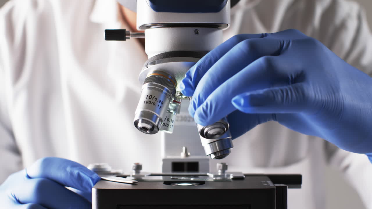 백색 배경에 복사 공간을 가진 실험실 현미경을 사용하는 남성 과학자의 클로즈업 비디오