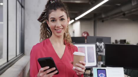 mujer creativa biracial feliz usando teléfono inteligente en una oficina casual, en cámara lenta