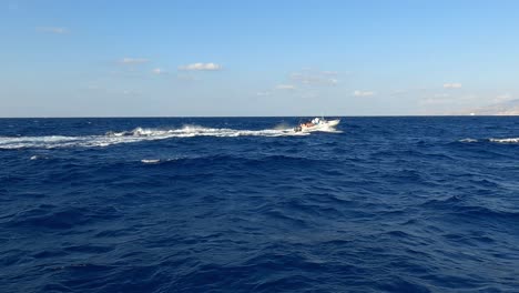 dinghy rubber boat with tourist on board navigating on sea water at high speed leaving white wake trail seen from another cruising vessel