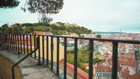 Lisbon-hill-viewpoint-through-fences-to-roofs,-castle-and-river