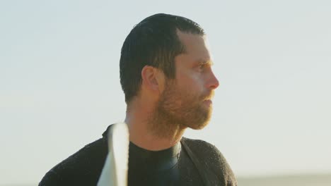 side view of mid-adult caucasian male surfer with surfboard standing at beach during sunset 4k