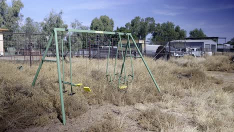 columpio abandonado en el césped seco rural cubierto de vegetación