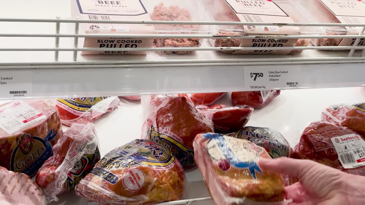 Close-up of hands examining various packaged meats on a supermarket shelf.