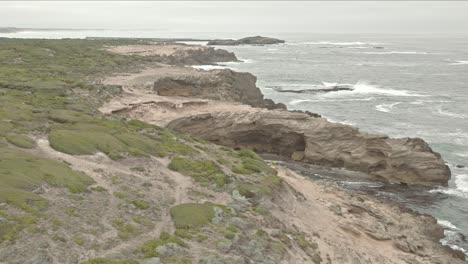 Reverse-flying-over-jagged-coastline-as-strong-unrelenting-waves-smash-on-rocks