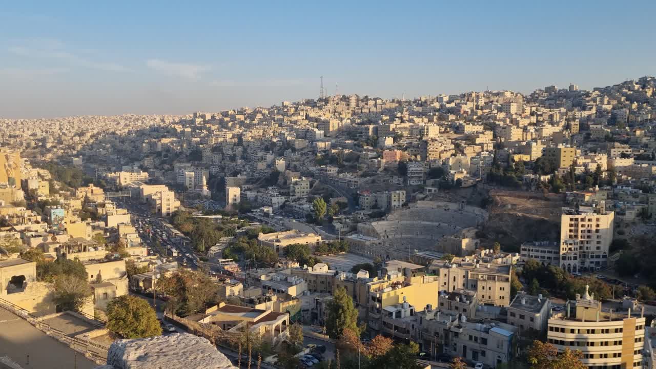 Tramonto mozzafiato su Amman, in Giordania, con una calda luce dorata che illumina i tetti della città e l'antico teatro romano, evidenziando la fusione tra punti di riferimento storici e vita urbana