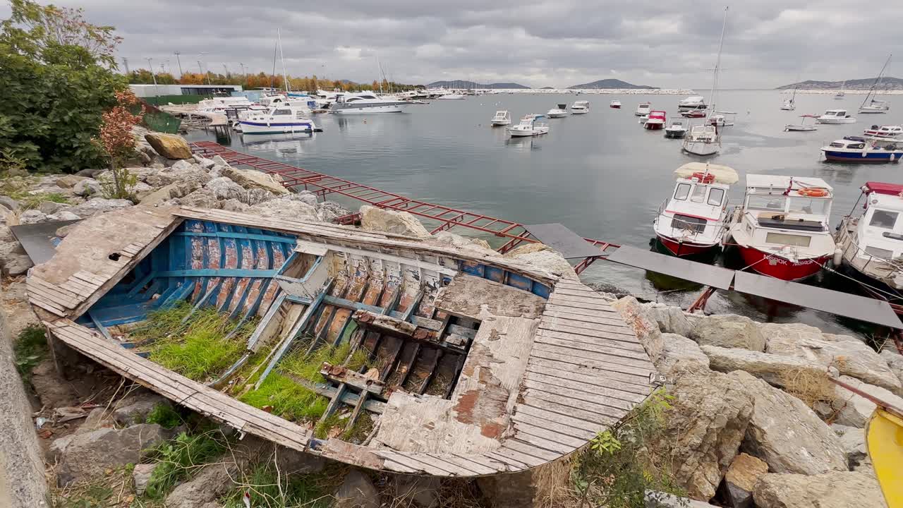 Scrap wooden row boat standing on the rocks on the sea shore in autumn in cloudy weather.