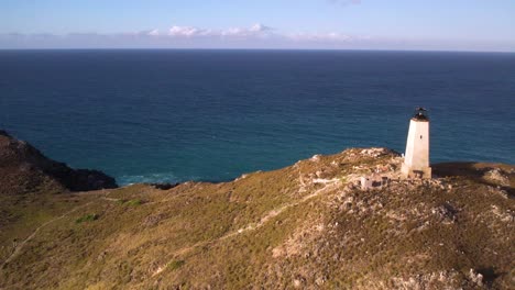 Aerial-view-of-a-small-lighthouse-located-on-a-rock-offshore-from-a-tropical-beach