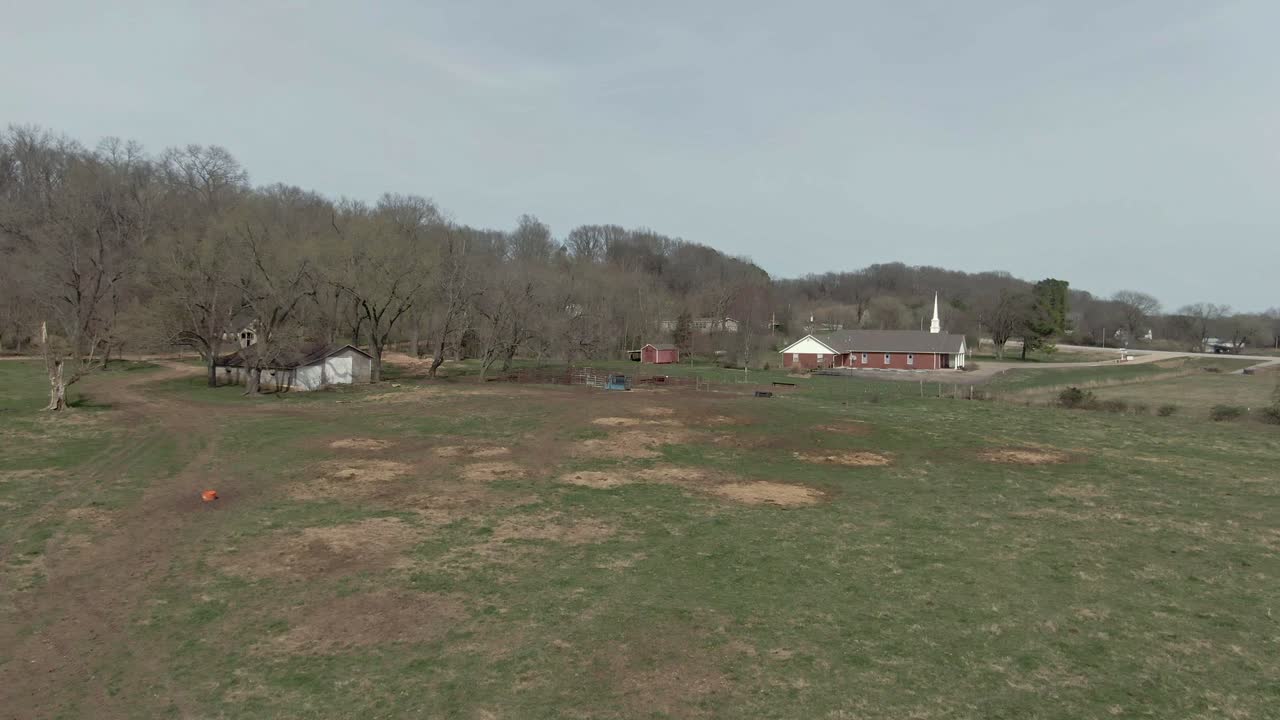 low altitude aerial view of baptist church beside farm house in the pasture