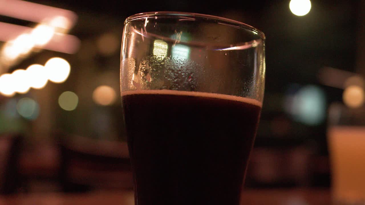 Un bicchiere di birra scura stout è appoggiato su un tavolo di legno in un bar poco illuminato