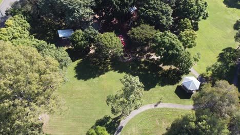 Drone-ascending-over-a-green-park-with-children's-playground-and-shady-trees