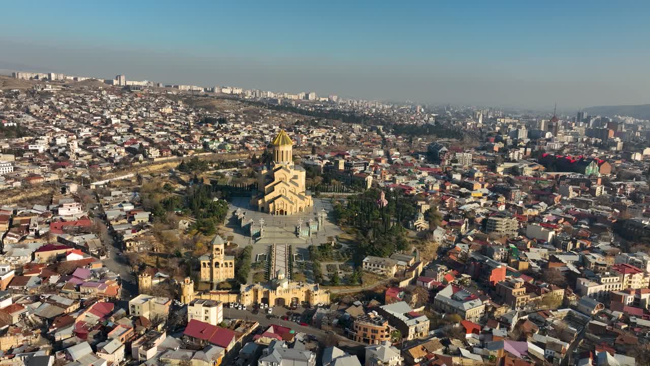 Drone della Cattedrale della Santissima Trinità (Sameba) a Tbilisi, in Georgia, circondata da case residenziali e immersa nella calda luce del sole serale, mette in risalto uno dei monumenti più iconici della città.