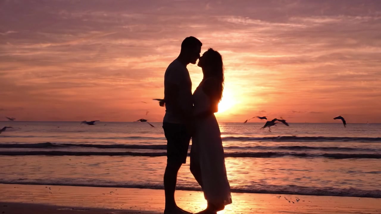 A Romantic Sunset Walk on the Beach: A Couple Holds Hands as They Stroll Together, Transitioning into a Tender Embrace Against a Stunning Sunset Backdrop