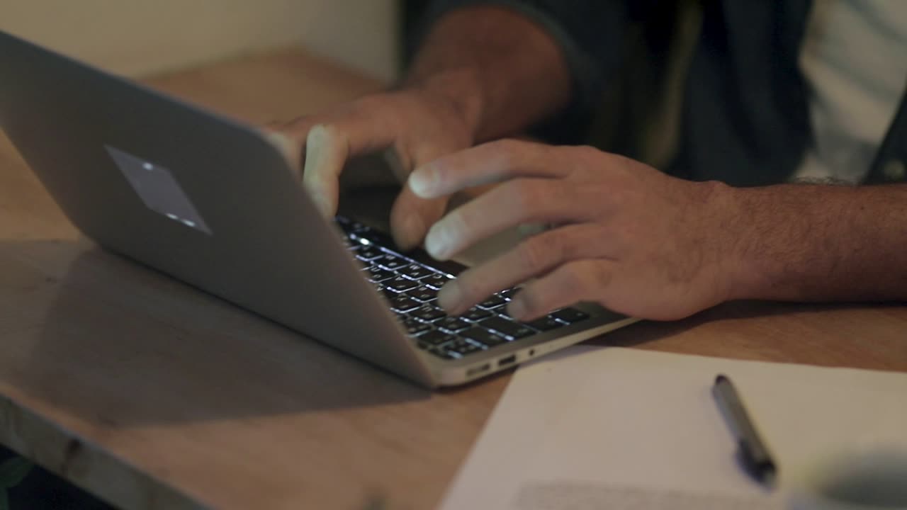 manos masculinas escribiendo en una computadora portátil en una cafetería