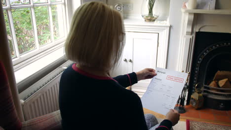 an unrecognizable senior woman worried about debts opening a debt letter