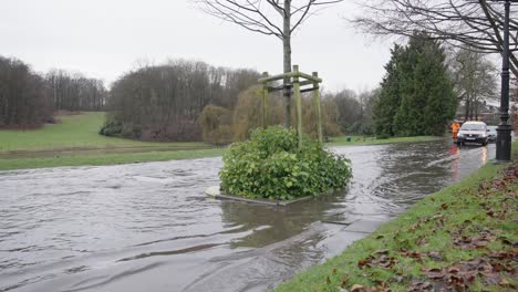 A-repair-team-in-orange-outfit-arrives-at-the-flooded-street-while-car-drives-through-the-water-puddle