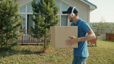 Happy delivery worker carrying cardboard box and enjoying music in headphones dancing having fun