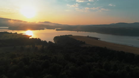 Un-Hermoso-Amanecer-Sobre-Las-Montañas-Y-Un-Lago-Que-Refleja-El-Amanecer,-Hay-Una-Niebla-Baja-Al-Lado-Del-Lago