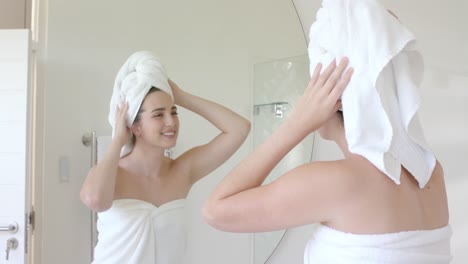 feliz mujer caucásica mirando frente al espejo con una toalla en la cabeza en el baño en cámara lenta