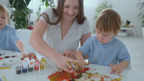 Mom-helps-her-son-to-make-a-handprint-on-paper-using-paint.-Joint-leisure-matter-of-the-child.-Happy-and-caring-mom