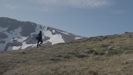 Wide-Shot-of-Woman-Walking-Along-Scotland-Mountain-Ridge-with-Subtle-Sun-Flare