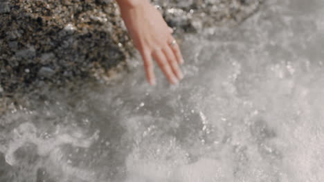 Cerrar-La-Mano-De-Una-Mujer-Tocando-Olas-De-Agua-Salpicando-A-Un-Turista-De-Vacaciones-Disfrutando-De-Un-Hermoso-Día-En-La-Playa