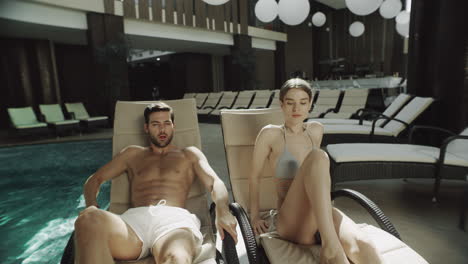 Closeup-beautiful-couple-lying-on-loungers-near-pool-indoor.