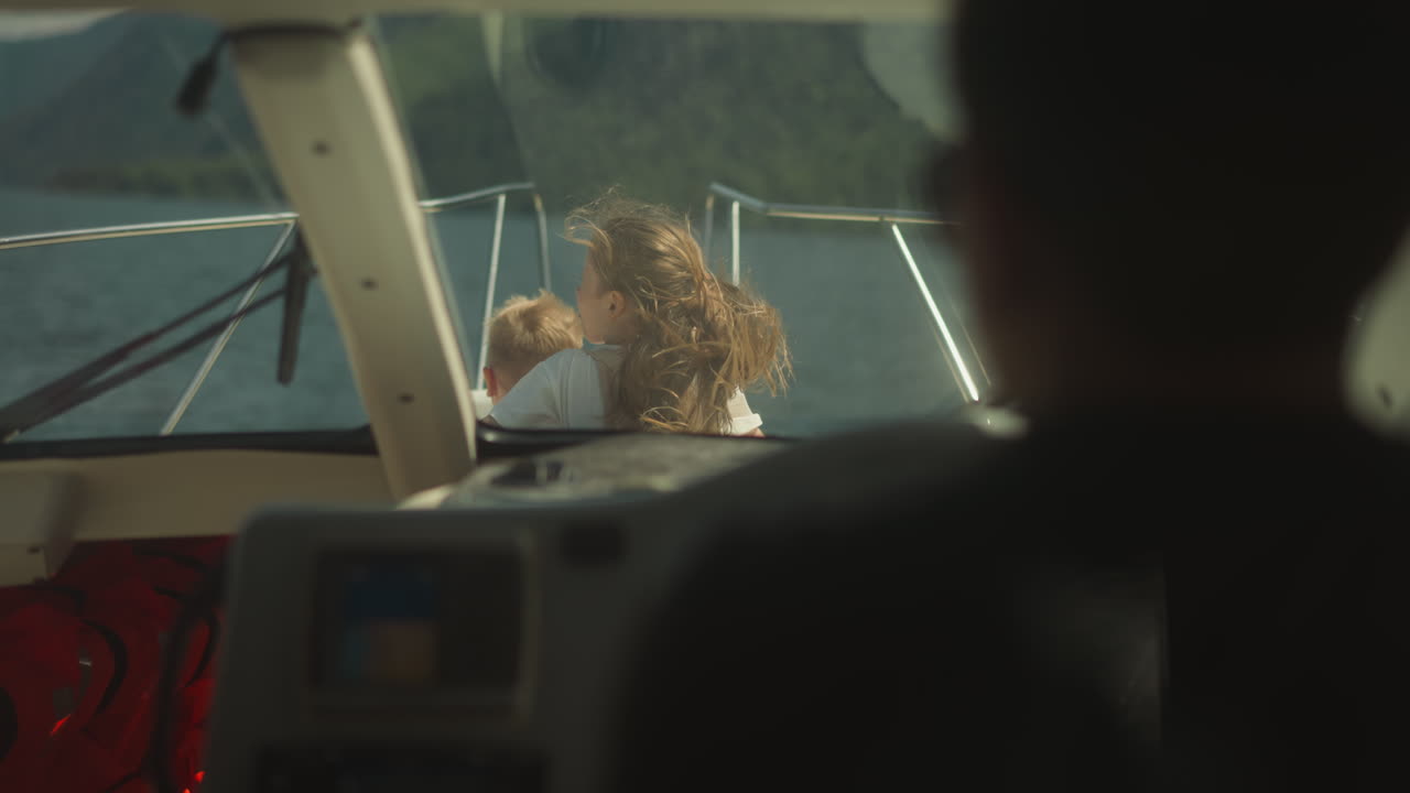 niña con cola de caballo y niño pequeño toman el sol en el velero vista de la cubierta de proa desde la cabina del capitán. niños tranquilos disfrutan del paisaje marítimo en un yate de vacaciones