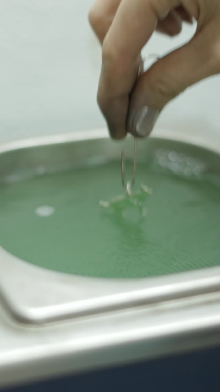 Close-up of a hand dipping an object into a green liquid