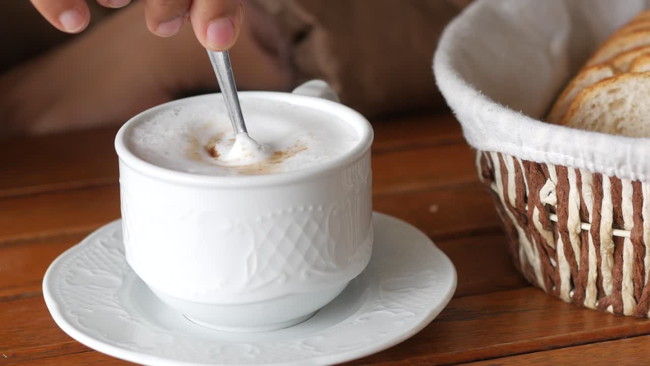 Person enjoying a cappuccino and bread at a table