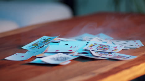 pile of playing cards on a wooden table with smoke