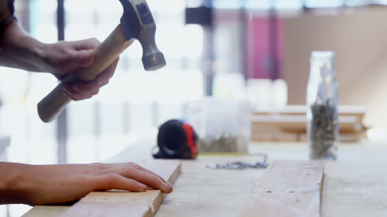 Female welder hammering nail on a wooden plank 4k