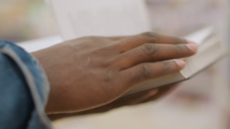 close-up of hand gently holding book's edge, fingers resting on pages, showcasing detailed skin texture and soft focus, with blurred background, emphasizing focus and calm reading atmosphere