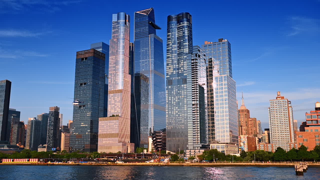 Nova Iorque, EUA, 1 de abril de 2026: Horizonte de Hudson Yards com helicóptero sobre o Rio Hudson. Torres modernas de Hudson Yards, helicóptero, Rio Hudson em primeiro plano, céu azul, luz lateral quente