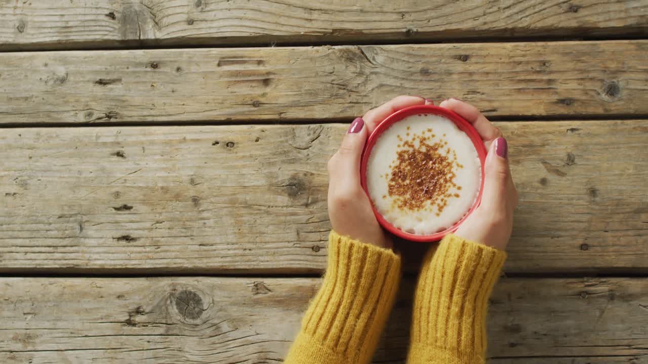 Video delle mani di una donna caucasica che tiene una tazza di caffè su una superficie di legno