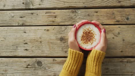 Video-of-hands-of-caucasian-woman-holding-mug-with-coffee-on-wooden-surface