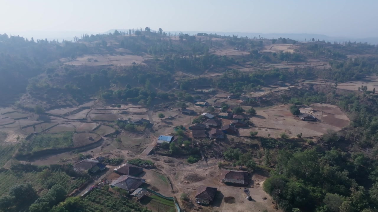 Pemukiman desa terpencil di Vansda, Gujarat, India, menunjukkan rumah-rumah yang tersebar dan lahan pertanian di seluruh medan berbukit. Bidikan drone maju perlahan bergerak mendekat ke rumah-rumah tradisional pedesaan.
