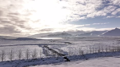 drone swiftly approaches a snowy icelandic valley with trees, mountains, and fjord in the distance.