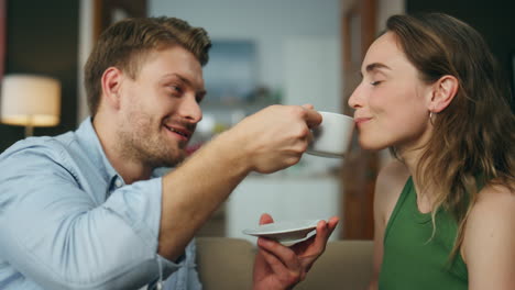 Sanfter-Mann-Behandelt-Frau-Mit-Einer-Tasse-Kaffee-Auf-Der-Couch,-Nahaufnahme.-Paar-Trinkt-Espresso