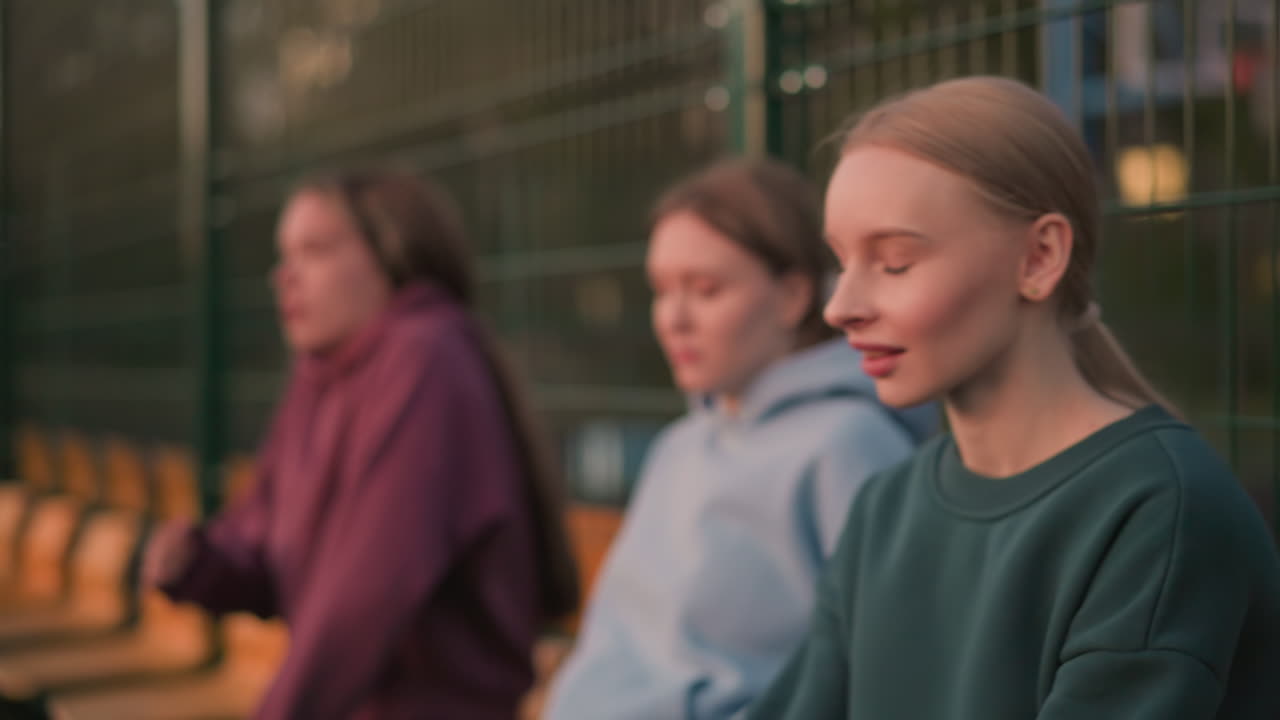 운동선수들이 긴 훈련을 마치고 휴식을 취하고, 초록색 옷을 입은 한 여인이 머리를 숙이고, 다른 선수들이 에 앉아서, 야외에서 강렬한 운동을 한 후 휴식을 취하며 회복하고 있습니다.