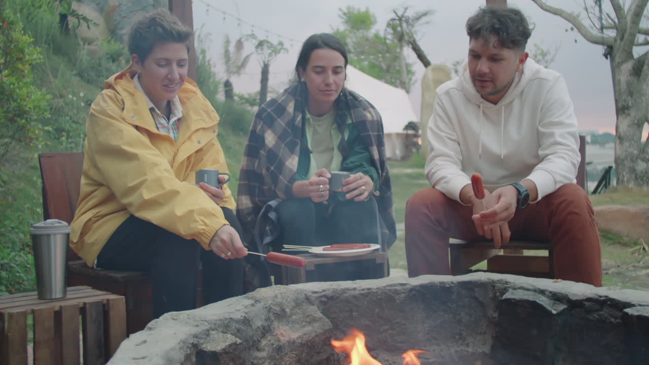Company of Tourist Talking and Cooking Food over Campfire