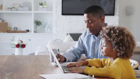 Pre-teen-African-American-girl-sitting-at-a-table-working-on-a-laptop-computer-with-her-home-tutor,-side-view