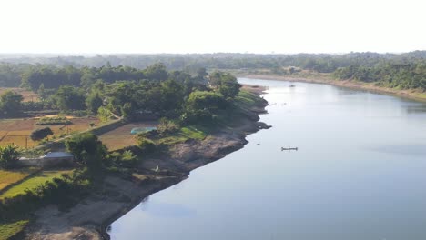 A-rural-village-on-the-banks-of-Surma-river,-with-a-fishing-boat-and-a-traditional-farmer's-house,-showcasing-the-beauty-of-countryside-living