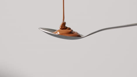 close up of melted chocolate being poured onto spoon and overflowing against white background with copy space