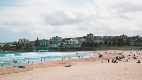 Timelapse-of-people-on-Bondi-Beach's-south-end-during-summer,-with-Icebergs-in-the-background