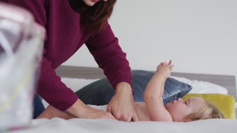 madre caucásica cambiando el pañal de su bebé en la cama en casa