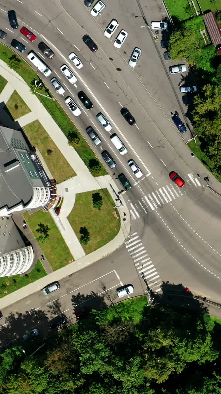 Cars driving on road. Traffic movement among green trees and modern buildings in the city. Panoramic shot of the city highway. Top view. Vertical video