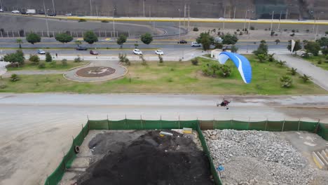 Drone-video-of-a-paraglider-smoothly-landing-on-a-dirt-track-in-Lima,-Peru