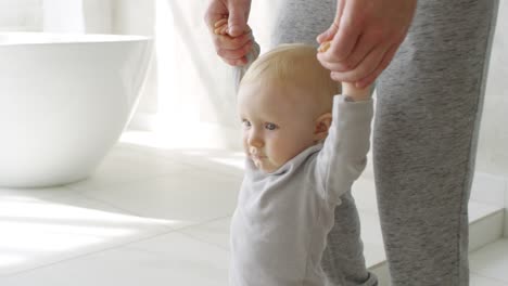 Unrecognizable-Father-Holding-Arms-Of-Adorable-Baby-Boy-Learning-To-Walk-In-Bathroom